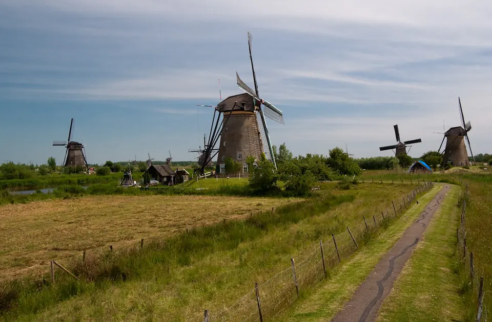 Molens van Kinderdijk onder een blauwe lucht met sluierwolken, naast groen grasland en een kronkelend fietspad.